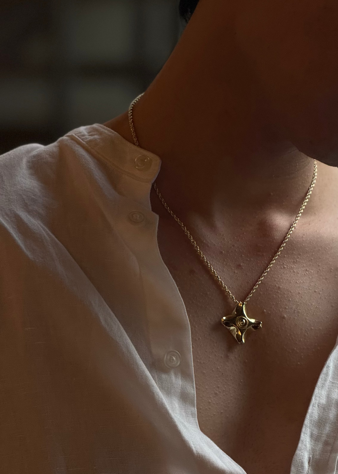 A close-up lifestyle shot of a man wearing apex gold chain pendant  paired with an open white button-down shirt.